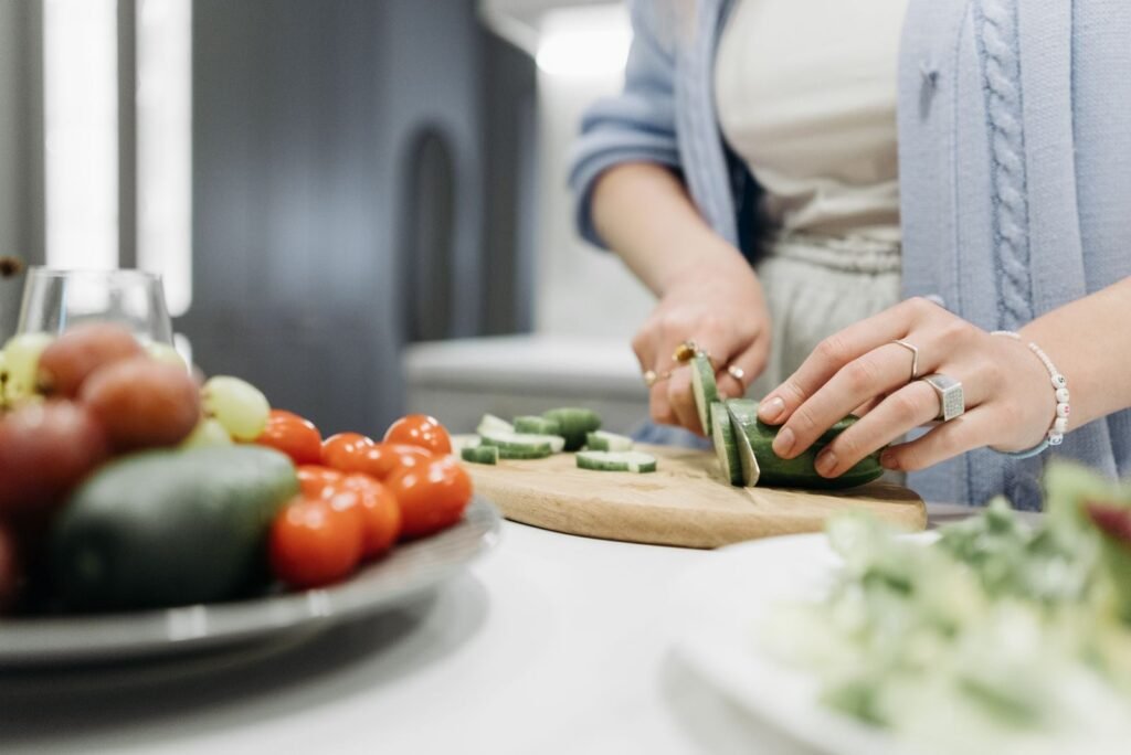 Close-up of a woman slicing cucumbers on a wooden board surrounded by fresh vegetables.